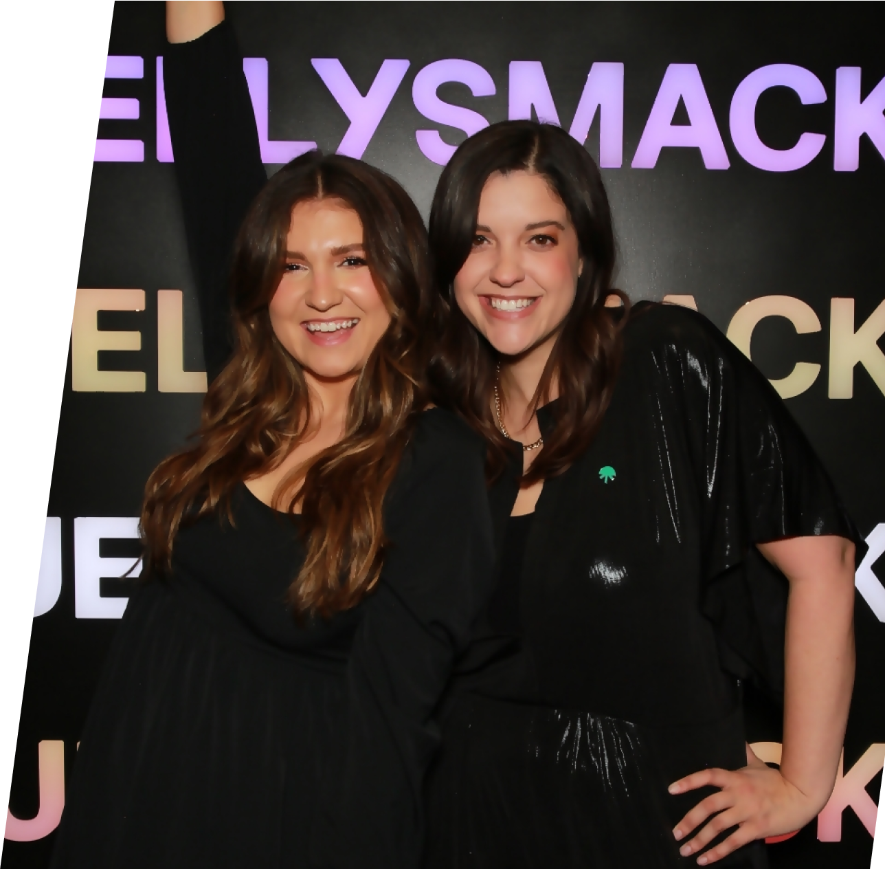 Two female Jellysmack employees smiling and posing in front of step and repeat Jellysmack backdrop. 