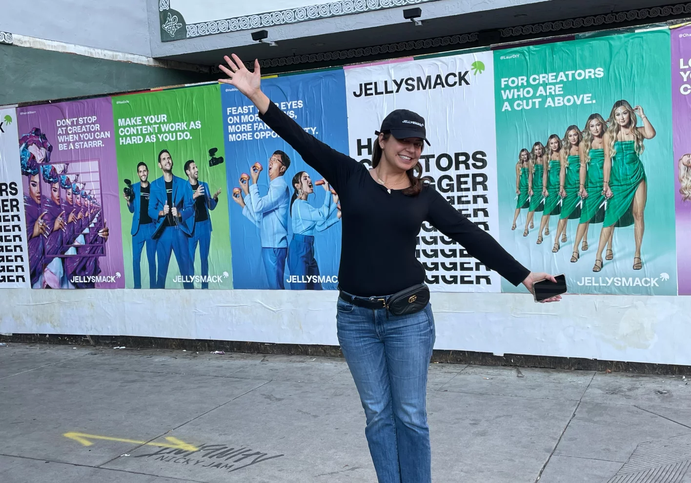 Woman smiling with her arms extended while standing on the sidewalk in front of Jellysmack advertisements.