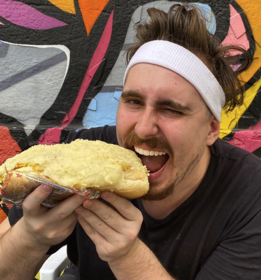 Close-up shot of YouTube creator Gaba about to take a bite of a large bread in front of a colorful background.  