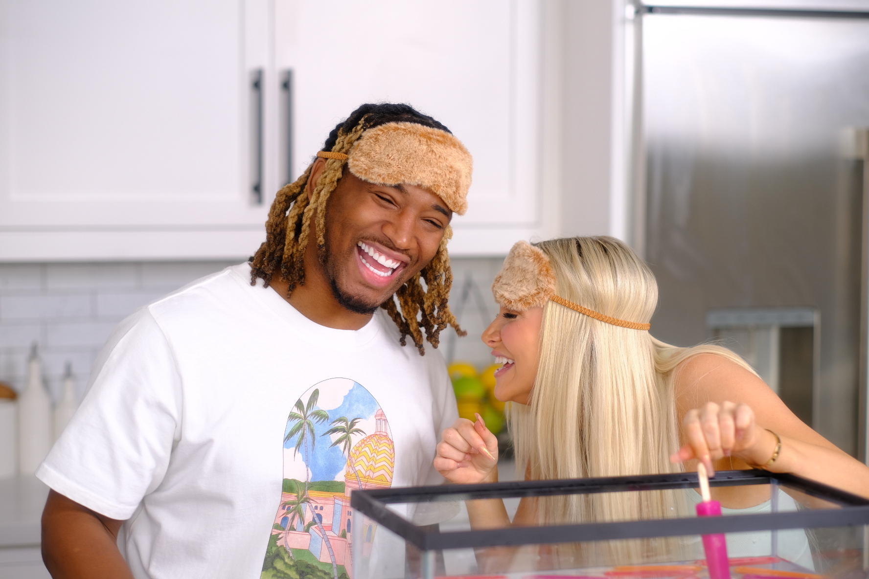 Couple content creators Charles & Alyssa in a kitchen setting while Alyssa holds a tray while the creators laugh