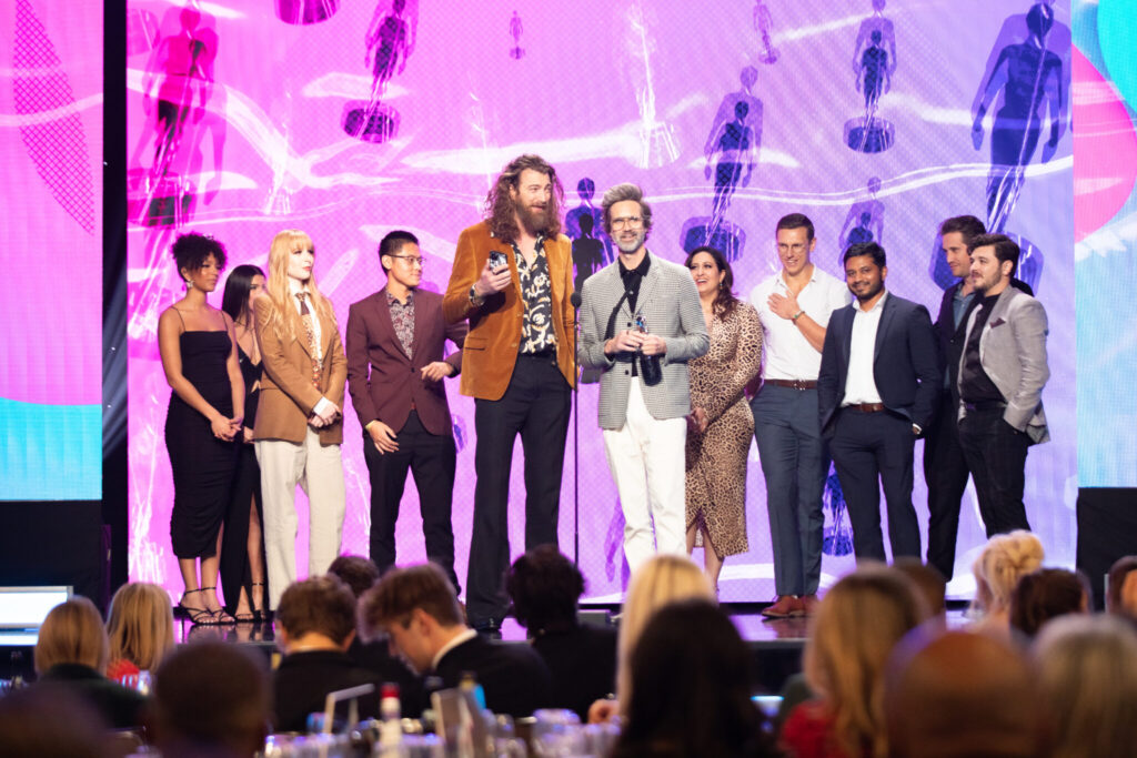 Creators give acceptance speech on stage at the 2022 Streamy Awards with colorful background.