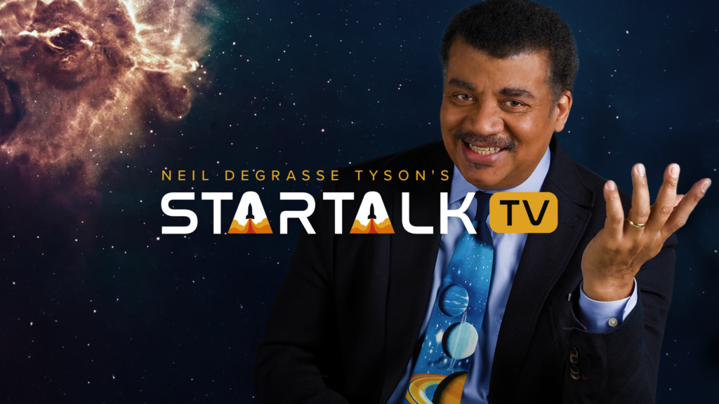 Astrophysicist Neil deGrasse Tyson smiling with hand gesturing in front of a galaxy background.